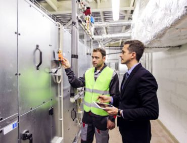 Worker and manager in electrical switchgear room of CNC plant